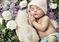 Śpiące niemowlę w uroczej czapeczce wśród fioletowych kwiatów