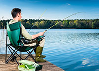 Mężczyzna siedzi na krzesełku nad rzeką i łowi ryby