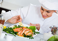 Uśmiechnięta kobieta w stroju szefa kuchni ozdabia potrawę