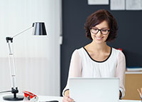 Uśmiechnięta kobieta w okularach pracująca na komputerze