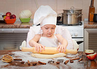 Dziewczynka w czapce szefa kuchni wałkuje ciasto