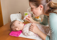 Kobieta oczyszcza niemowlakowi nosek przy pomocy aspiratora