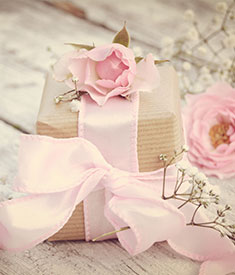 Prezent z różową kokardą ozdobiony kwiatami