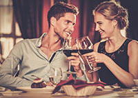 Para w trakcie kolacji, stukająca się kieliszkami z czerwonym winem